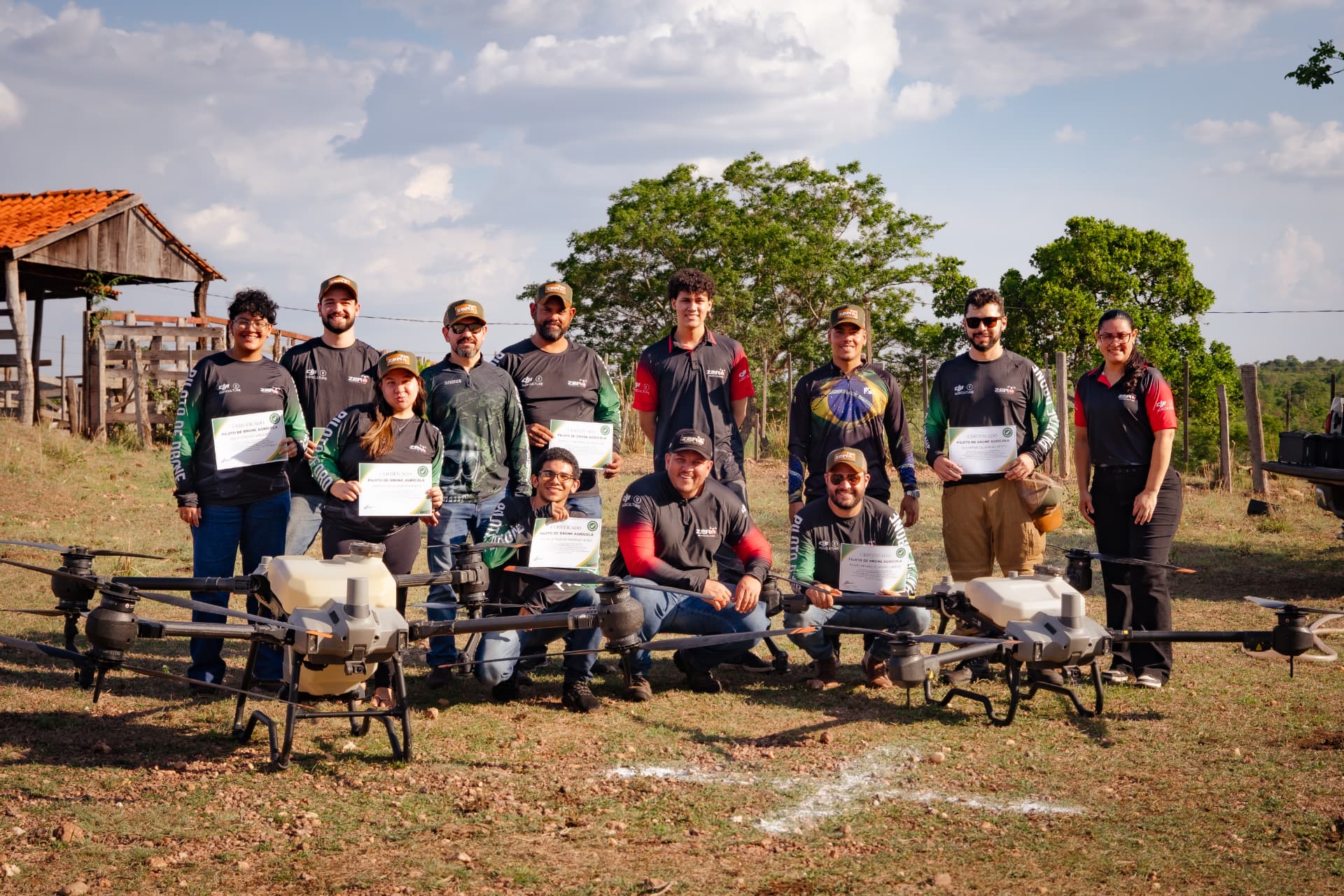 Equipe e alunos da Zero65 Drones com certificados, reunidos entre drones agrícolas em campo